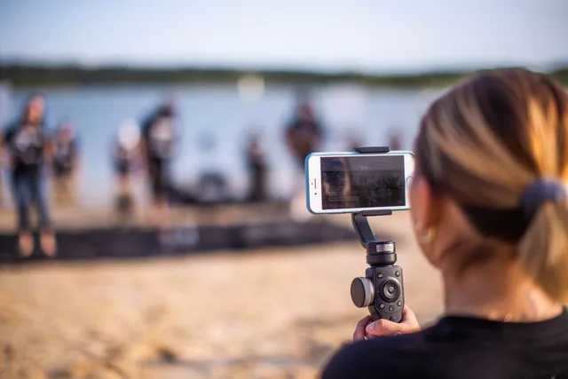 Unrecognizable female using smartphone to record video of band during music show on beach. UGC marketplaces and advertising rules: checking one advert for recognition, claims and rights