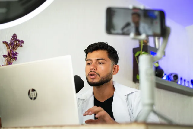 A young man works on a laptop while streaming content online with a smartphone. UGC marketplaces benchmark research in England: no official figure to cite