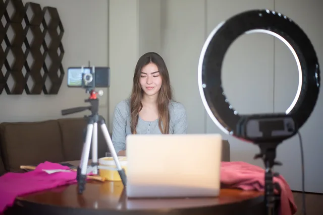 A young woman vlogging indoors using a smartphone, tripod, and ring light setup. UGC marketplaces in England: what providers must prove