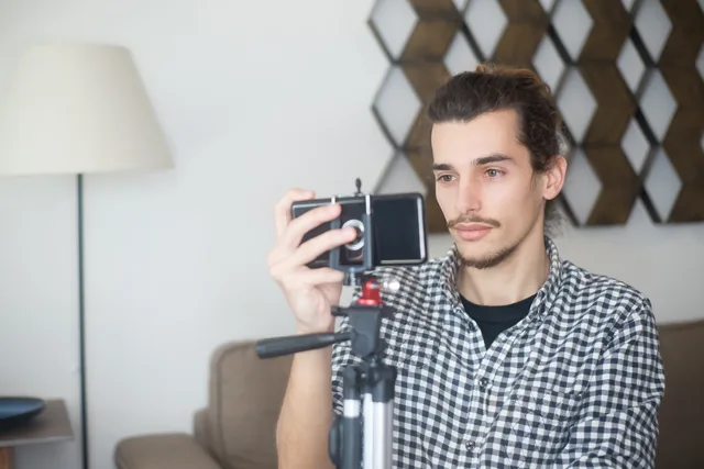 Young man with plaid shirt using a smartphone and tripod to create content indoors in Portugal. UGC marketplaces commercial contracts: seven review checks