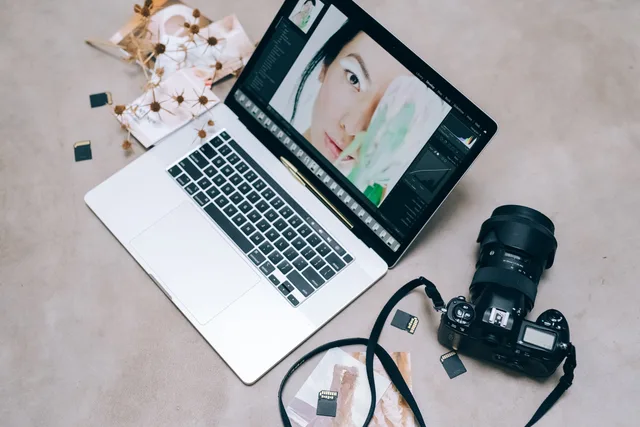 Flat lay of a laptop with photo editing software, camera, and memory cards on a desk. UGC marketplaces: how to run customer interviews that stay clear of sales