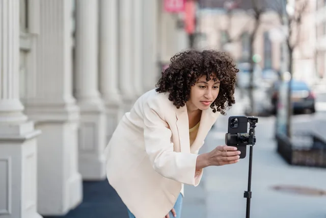 Attentive young ethnic female vlogger leaning forward to cellphone on tripod while preparing for video record in city. Personal data through one UGC commission, from lawful basis to deletion