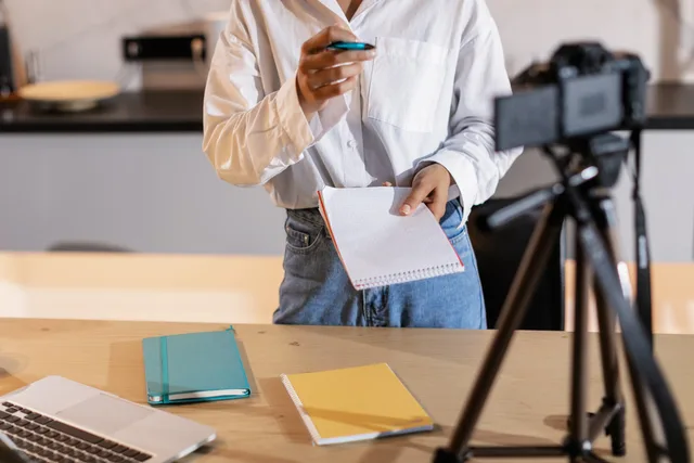 Vlogger recording content with a camera, holding notes and using a laptop in a modern setting. UGC marketplaces in England: what each market signal shows
