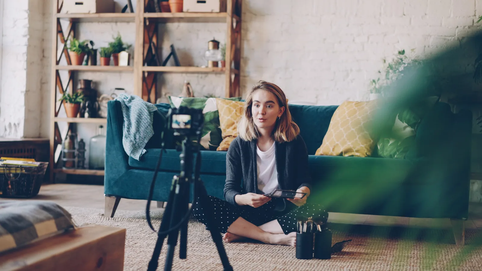 Woman filming vlog at home with camera setup, surrounded by plants and cozy decor.