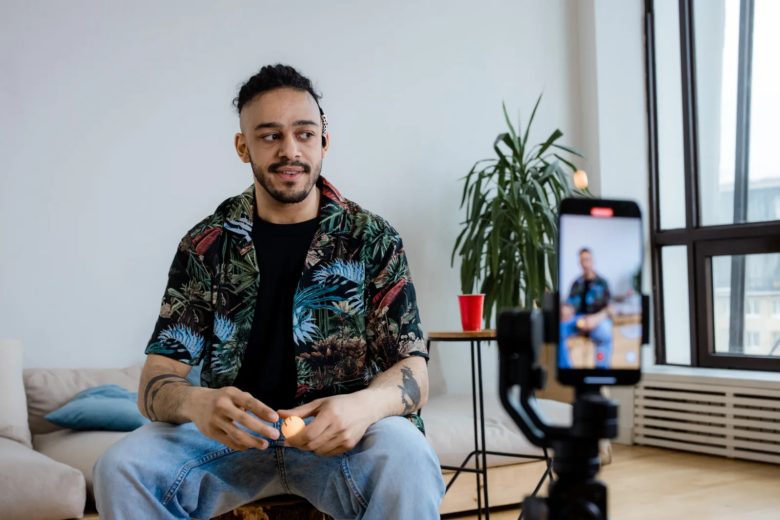 A young man recording video content indoors with a smartphone and tripod.