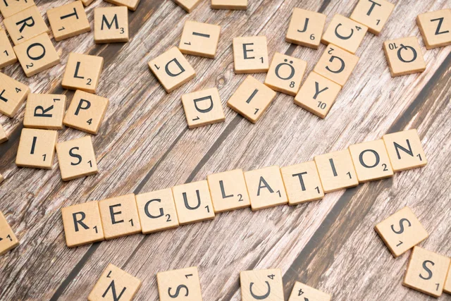 Wooden letter tiles spelling 'Regulation' on a textured wood background, conveying themes of compliance and structure. UGC marketplace team roles: eight accountabilities mapped to UK sources
